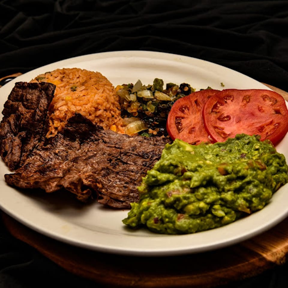 Mexican dish with grilled steak, rice, guacamole, sliced tomatoes, and sautéed vegetables.