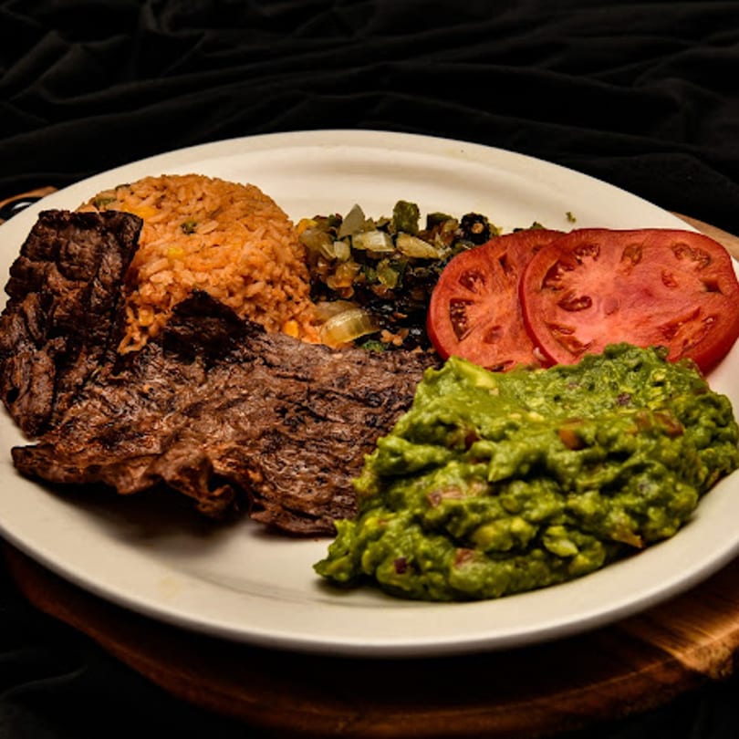 Mexican dish with grilled steak, rice, guacamole, sliced tomatoes, and sautéed vegetables.
