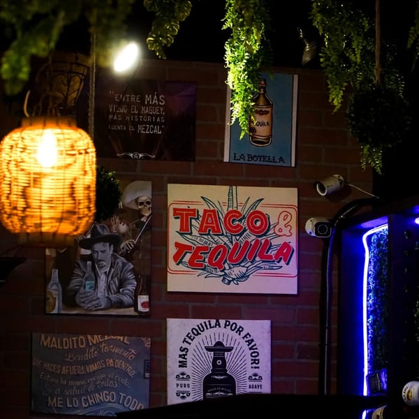 A dark brick wall with various Mexican-themed signs, including "Taco & Tequila" and a woven lantern.