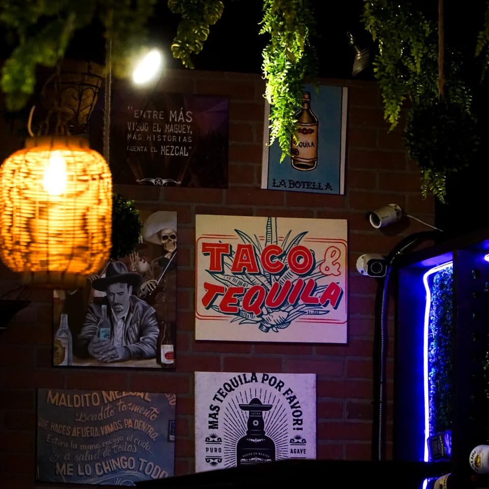 A dark brick wall with various Mexican-themed signs, including "Taco & Tequila" and a woven lantern.