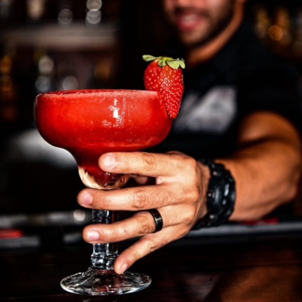 A hand holding a strawberry margarita with a fresh strawberry garnish at Taqueria Jalisco Midland.
