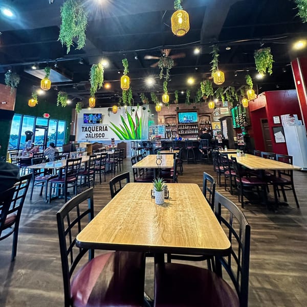 Interior of Taqueria Jalisco Midland, featuring dining tables, a bar, and hanging plants with warm lighting.