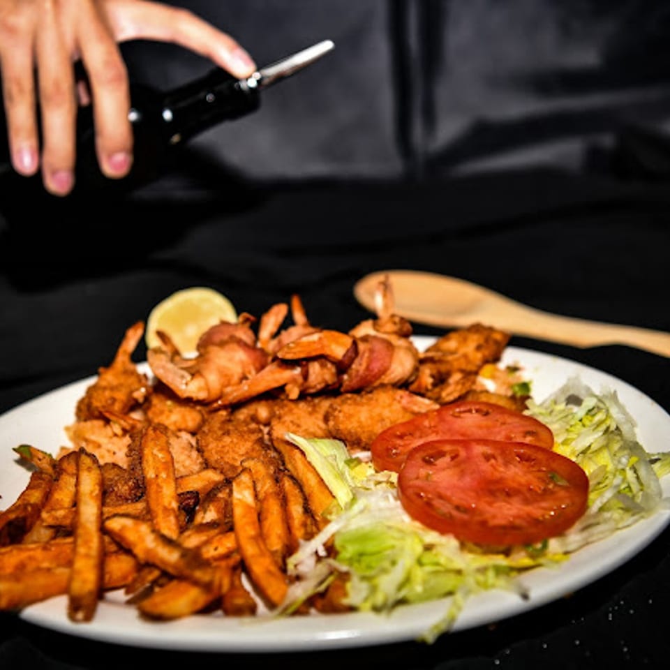 A plate of bacon-wrapped shrimp, fried shrimp, french fries, and a side salad with lemon.