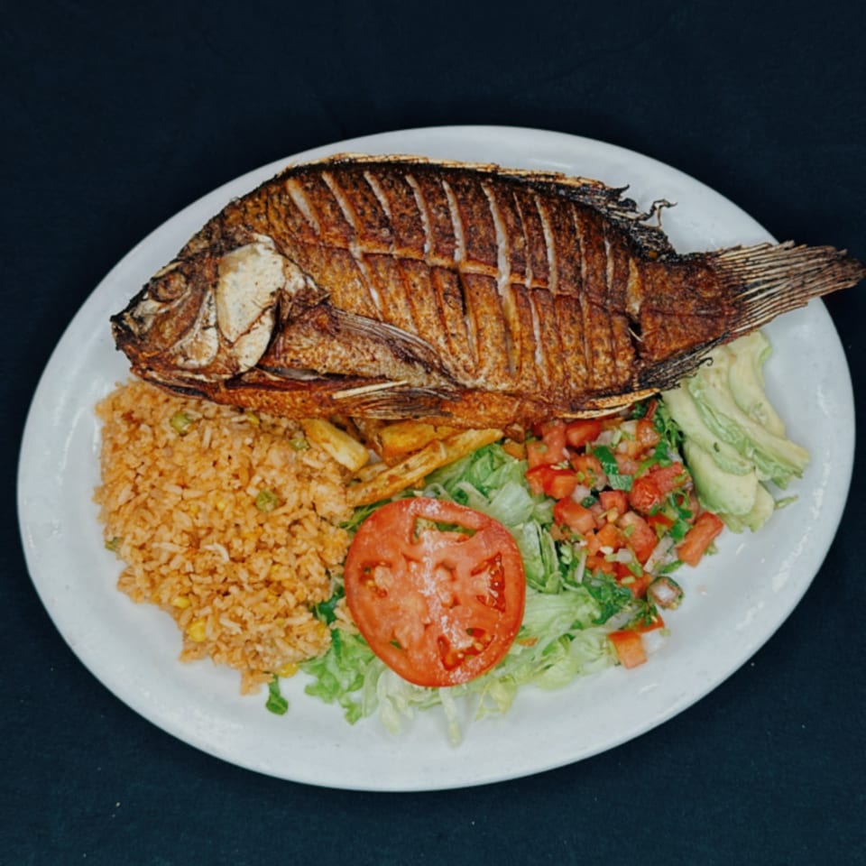 Whole fried fish with rice, fries, sliced avocado, and a fresh salad with tomato.